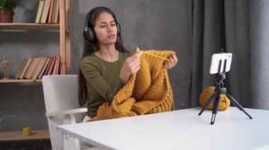 Bir kadın evdeki koltukta otururken örgü örüyor. Bayan örgü örmeyi öğreten bir video kaydediyor. Kadın nakış işi. Bir yaşam biçimi olarak örgü örmek.