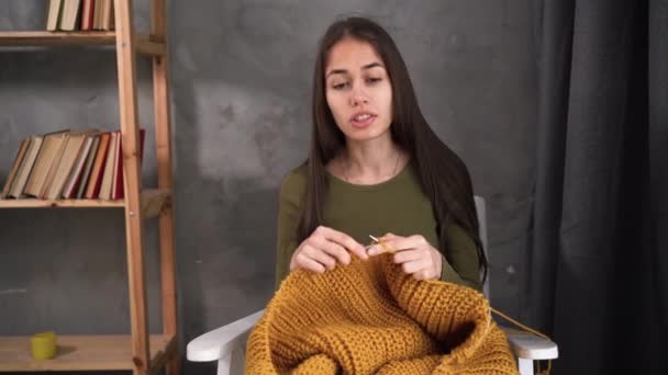 A young girl knits a warm sweater in front of a laptop. She teaches online students the art of knitting. An experienced teacher uses two webcams to help students learn. — Vídeos de Stock