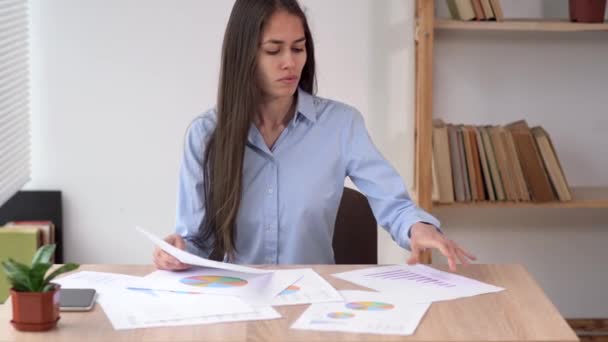Pandangan close-up tentang seorang wanita bisnis muda yang bekerja di sebuah interior kantor di atas meja, melihat pada lembar grafik. — Stok Video