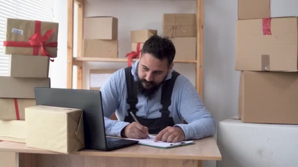 Propriétaire de petite entreprise indienne écrivant une commande en ligne à l'aide d'un ordinateur portable tout en travaillant au bureau à domicile avec des boîtes à cartes, entreprise en démarrage, télémarketing et expédition des commandes, PME — Video