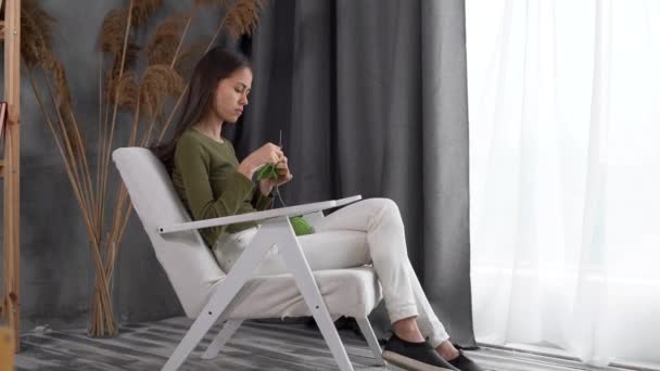 Mujer latina creativa joven tejiendo ropa y accesorios, disfruta de pasatiempo, agujas de tejer, utiliza hilo de cinta. crea detalles decorativos exclusivos hechos a mano mientras se relaja en un sillón — Vídeos de Stock