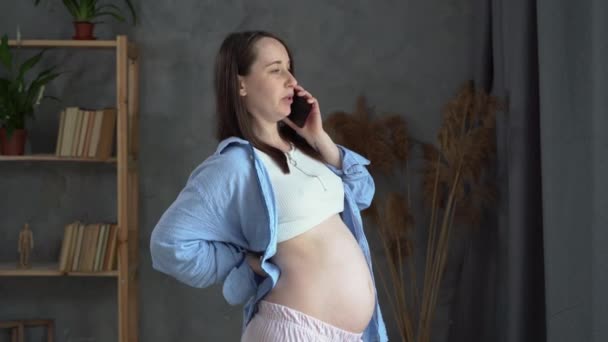 Real young pregnant woman talking on mobile phone, consulting doctor, contraction back pain, calling from home, pregnancy and surrogacy — Stock video