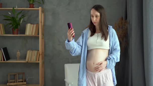 Pregnant caucasian woman standing in the room having a video conference with a doctor on a mobile phone, online communication, a pregnant expectant mother making a video call with a smartphone — Vídeo de Stock