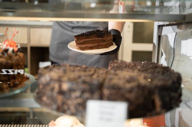 Çikolatalı pasta ve bir dilim şekerli bir dükkan. Pasta gösterisi, güzel cam teşhir, alışveriş merkezindeki pastanede çeşitli tatlılar, şehir konseptinde popüler yemek işleri.