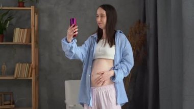 Hamile, beyaz bir kadın cep telefonuyla bir doktorla görüntülü görüşme yapıyor. İnternette iletişim kuruyor, hamile bir anne akıllı telefonuyla video görüşmesi yapıyor.