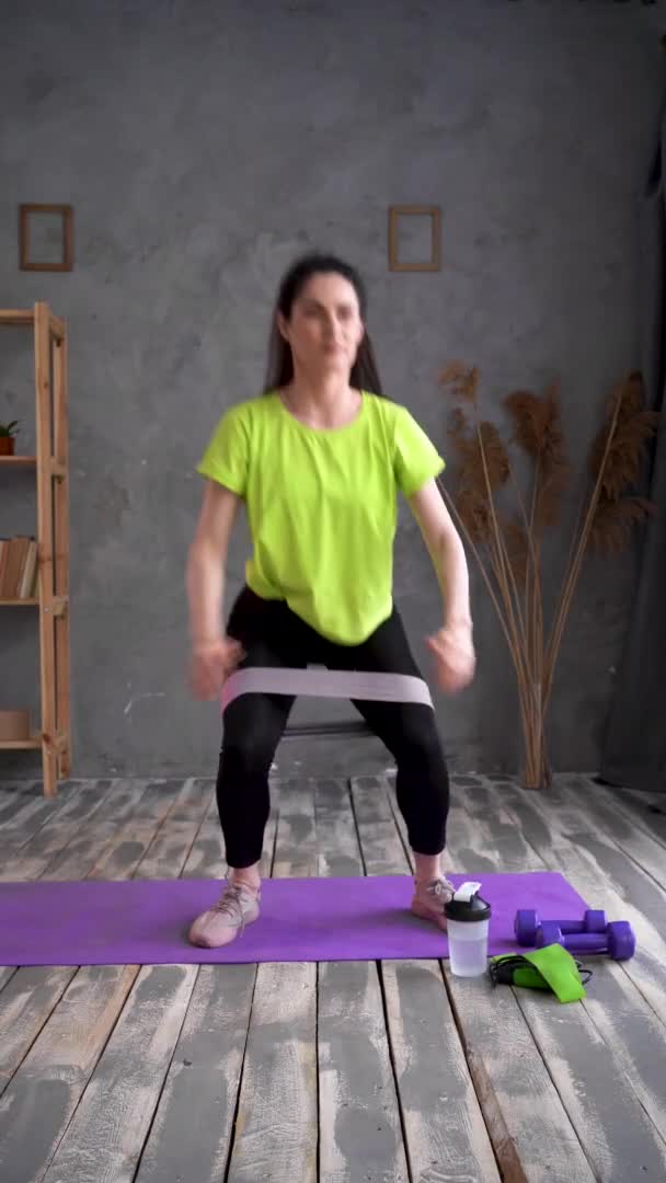 Sporty woman making squats using stretching strap, she is training at home. Fit girl is making fitness aerobic exercises in bedroom. camera in motion. Home fitness workout — Stok video