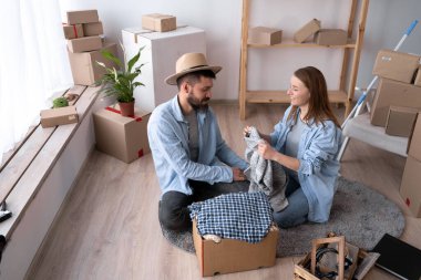 Taşındığı gün bir erkek ve bir kadın yere oturup eşyaları boşaltıyorlar. Yeni bir dairede mutlu bir çift. Ev kiralama ve satın alma kavramı. Boşluğu kopyala.