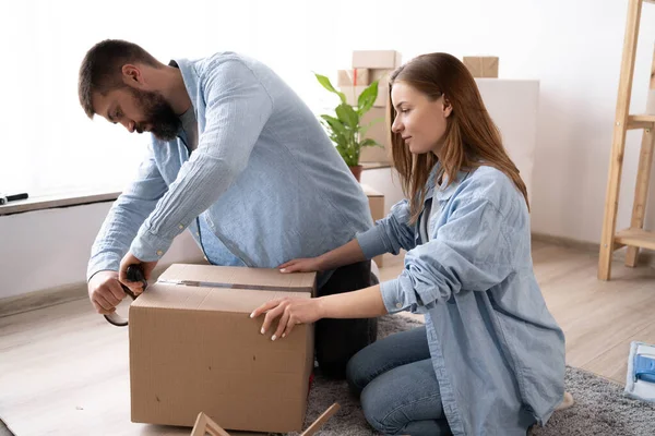 a man seals boxes ready for moving with scotch tape. couple in love packs things. copy space.