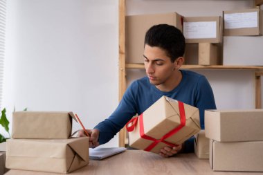 a working Muslim man in an online store. He wears casual clothes and packs goods for delivery. Muslim small business owners, packing goods into boxes, preparing them for delivery