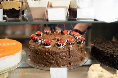 Bir kafenin camının arkasındaki vitrinde vişneli bir pastanın yakın çekimi. Boşluğu kopyala.