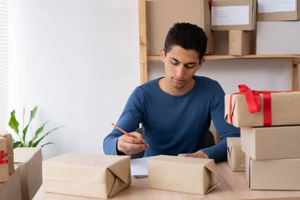 Online salesman young muslim salesman checks online order, checks goods in stock, package, mail delivery. arab man starts small business in home office. copy space.