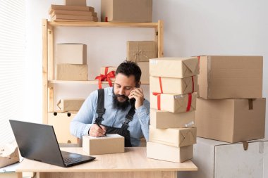 indian male business owners work from home online shopping, concept of entrepreneur and online trading. Sitting at home at the table in work overalls and writing the delivery address with a pen.