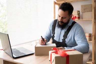 Evden online alışveriş yapan Hintli erkek işyeri sahibi girişimci ve çevrimiçi ticaret kavramı. İş yerinde iş tulumunda dizüstü bilgisayarla evde oturmak ve teslimat adresini yazmak.