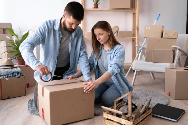 A man and a woman pack things on the day of the move. the guy seals the cardboard box with tape. copy space.