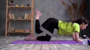 Ciddi atletik genç kadın evde bacak egzersizi yapıyor. Spor giyim sektöründe formda bir sporcu elastik lastik bantla ileri atlama egzersizi yapıyor.