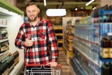 Süpermarkette alışveriş yapan yakışıklı bir adam, markette alışveriş arabası, su dolu beyaz bir adam, erkek alışveriş konsepti.