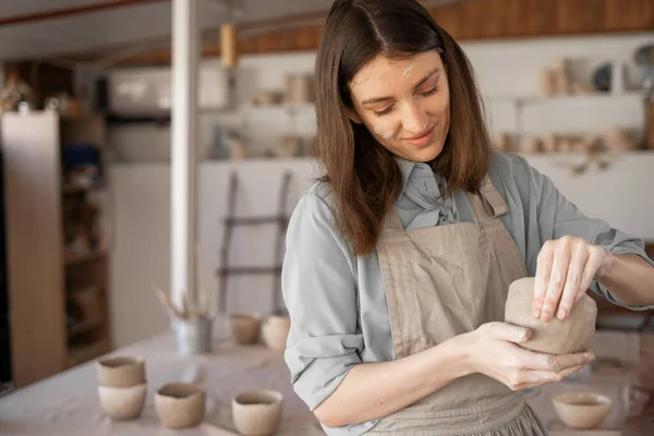 A young female ceramist prepares pottery in her studio. Hobby and leisure with pleasure, workshop, art concept.