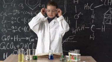 A little girl scientist in a white coat and goggles examines a test tube with a chemical reagent. Research and education at school.