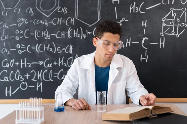 unidentified student in chemistry lab testing some unidentied chemicals, arabic chemist working at school, chemical experiment in classroom, young chemistry teacher sitting at table, chemistry science and learning