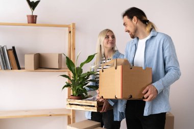 happy young couple carrying cardboard boxes and plant during moving to new apartment, man and woman of carrying boxes to new house on moving day, copy space