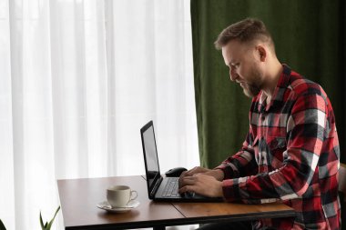 handsome young man freelancer using laptop working from home, studying online, guy typing on pc laptop surfing internet, looking at screen, enjoying remote work sitting at table, view profile