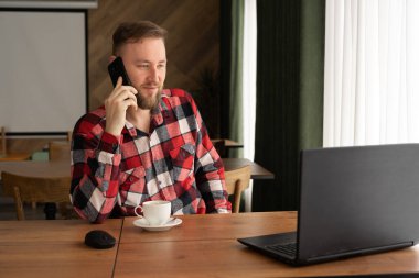 Smiling handsome businessman talking to his clients while working at home office using laptop, freelancer drinking coffee in cafe