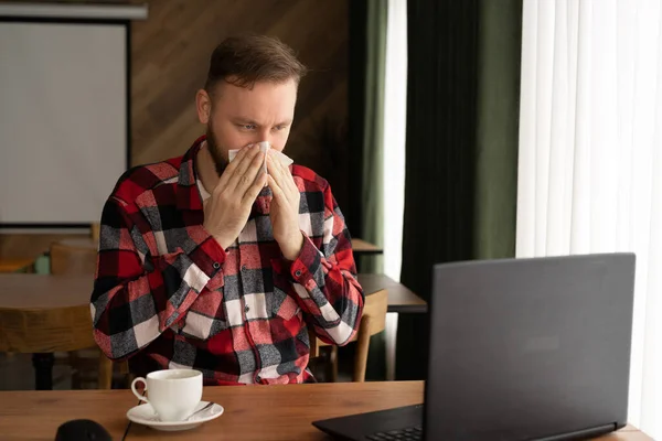 selective focus of businessman sneezing in tissue while looking at laptop in home office or cafe, freelancer allergic or flu, wipe your nose with a tissue