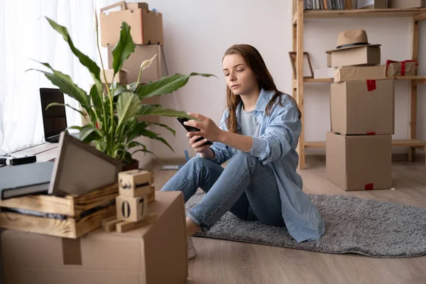 搬家的日子家庭搬出公寓移动盒的妇女使用在线移动服务的手机应用程序 很容易拿起与新家的包 白种人新房主女孩坐在地板上 — 图库照片