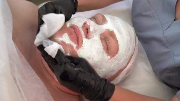 Cosmetoloog verwijdert gezichtsmasker met servetten in spa schoonheidssalon, man die anti-aging gezichtsprocedures, huidverzorging en cosmetologie — Stockvideo