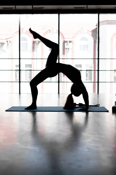 silhouette yogi woman exercising exercising doing Wild Thing, Flip-the-Dog exercise, Camatkarasana pose, exercising in the gym on the background of the window, sportswear, healthy lifestyle concept.