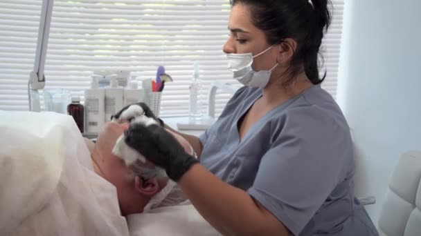 Μάσκα προσώπου σε spa σαλόνι για τον άνθρωπο, θηλυκό cosmetologist αφαιρεί αναζωογονητική μάσκα από τον πελάτη χρησιμοποιώντας μαντηλάκια, περιποίηση προσώπου δέρμα — Αρχείο Βίντεο