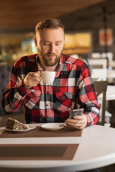 happy young man with smartphone and coffee cup texting at city cafe, business, technology and people concept