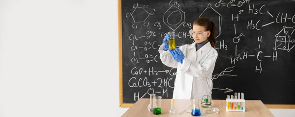 funny scientist child with glasses in lab coat with chemical flasks having an idea, school blackboard background with science formulas, banner, place for text