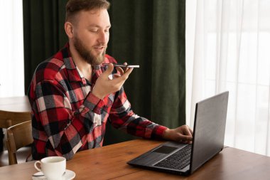 Beyaz adam akıllı telefonda ses asistanı kullanıyor ya da iş yerinde sesli mesaj kaydediyor. Boşluğu kopyala