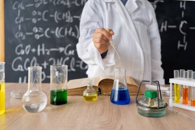 Kız öğrenci, fen dersinde cam parçalarını analiz edip karıştırarak kimyasal bir deney yapıyor. Eğitim ve bilim konsepti