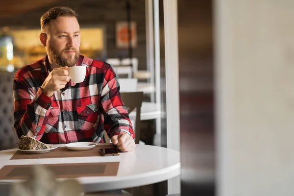 Handsome young caucasian man drinking coffee while sitting in a cafe. Caucasian man with a cup of coffee resting enjoying freedom. coffee break concept, looking at empty space