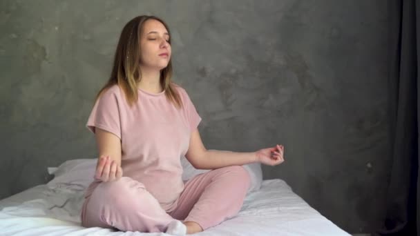 家で目覚めた後は朝ヨガの練習をしている若い妊婦さん ベッドの上に横足で座るヨギ女性モデルと瞑想 妊娠中の医療推進 — ストック動画