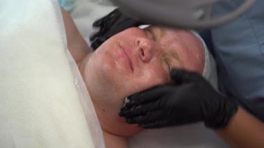 Erkeklerin yüz masajı, ovma, cilt temizleme, güzellik uzmanlarıyla randevuda bir adam. Kozmetik uzmanı spa salonundaki erkeklerin yüzüne kozmetik maske takıyor.