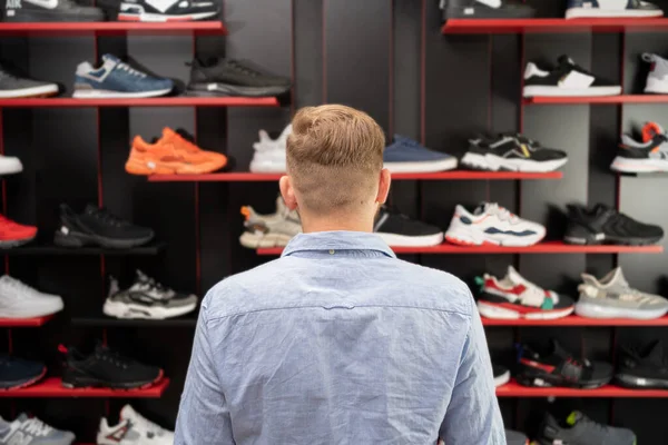 back view of man choosing hiking shoes while standing in modern sport shop, sports shoes department, copy space
