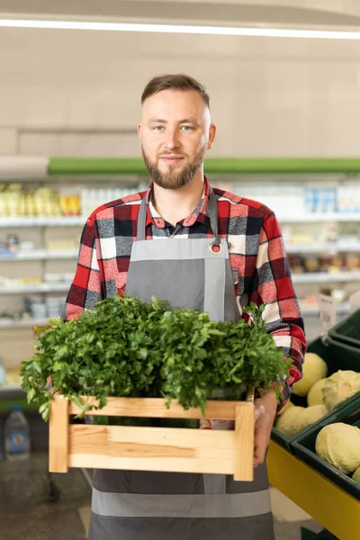 Portrait of smiling employee holding box of fresh vegetables and greens in supermarket, organic food concept