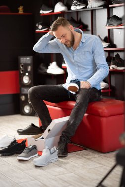 Beyaz sakallı adam modern spor mağazasının soyunma odasında otururken yürüyüş ayakkabısı seçiyor. Karmaşık bir seçim ve geniş bir çeşitlilik konsepti. Boşluğu kopyala.