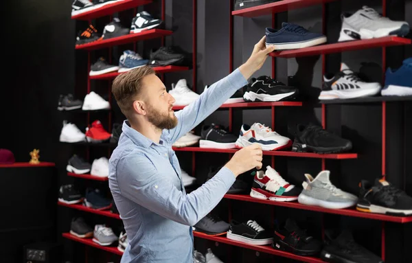 Man choosing sports shoes for running standing in the modern sportswear shop, shopper choosing sports sneakers in store