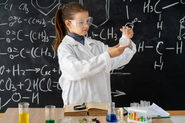 Beyaz önlüklü kız kimya laboratuvarında sıvı deneyleri yapıyor. Kimya dersi, eğitim ve bilim konsepti üzerine kimyasal deney yapıyor.