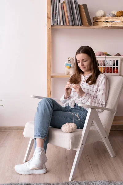 Woman knits crochet. girl sits on the armchair and knitting from yarn. Crochet thick threads. Home comfort. leisure and hobby concept