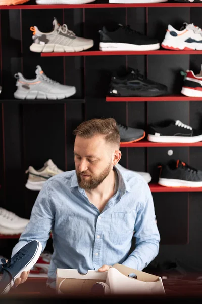 A man is shopping in a sporting goods store. The guy buys sneakers chooses the shoe model and size. Buying adventure shoes by a client. copy space.