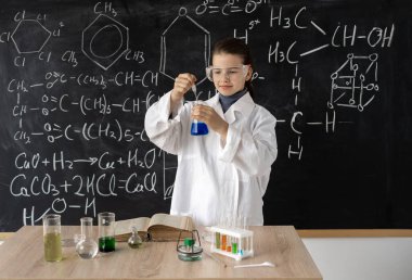 Laboratuvar önlüklü, kimyasal mataralı bilim adamı çocuk, bilim formüllü karatahta arka plan, okul konseptine geri dönüyor.