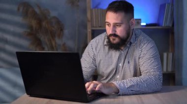 Genç, yakışıklı Hintli adam geceleri dizüstü bilgisayar kullanarak evde çalışıyor. Yaratıcı erkek sosyal medyayı kontrol ediyor, internette geziniyor.