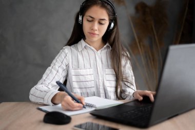 Evde dizüstü bilgisayar kullanarak kulaklık takan Latin kökenli kadın notlar yazıyor, kız üniversite öğrencisi öğreniyor ve online web siteleri izliyor, müzik dersleri dinliyor, e-öğrenim konsepti geliştiriyor.