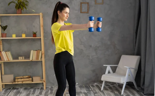 Beautiful young athletic woman in leggings crouches with dumbbells at home. Sport, healthy lifestyle concept