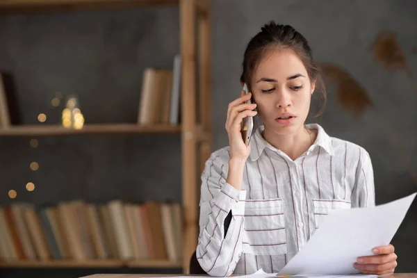 young hispanic woman with papers working at home office and calling on smartphone, serious businesswoman checking letter calling on sell phone sitting in the living room at home, copy space